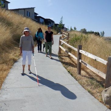 Photo of three women, two using white canes and one with a guide dog, walking down a trail.