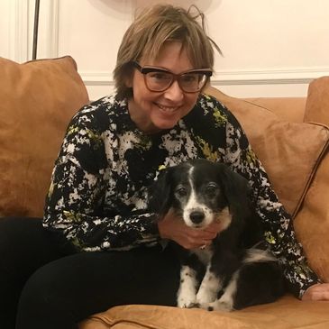 Woman smiling with her black and white dog on a brown couch.