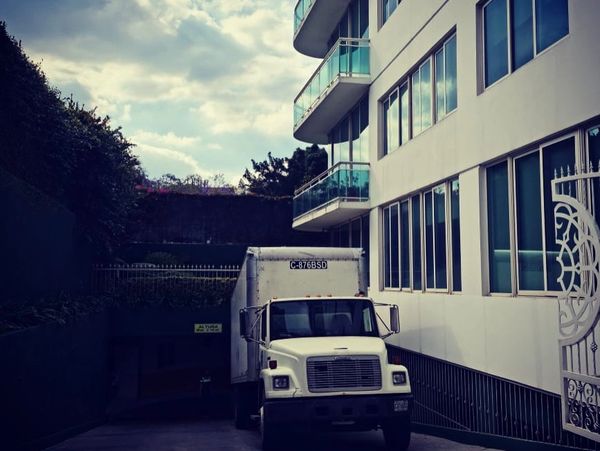 White delivery truck parked near a modern building under a cloudy sky.