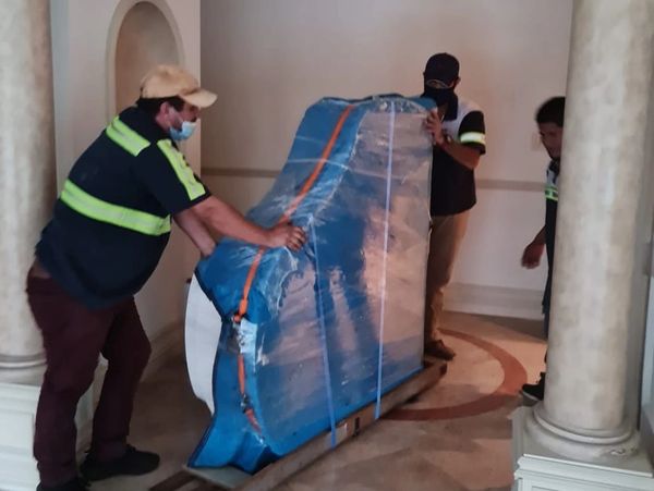 Three movers transporting a wrapped piano indoors.