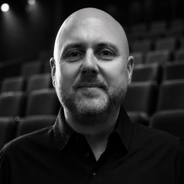 Portrait of a bald man with a beard in a dark shirt.