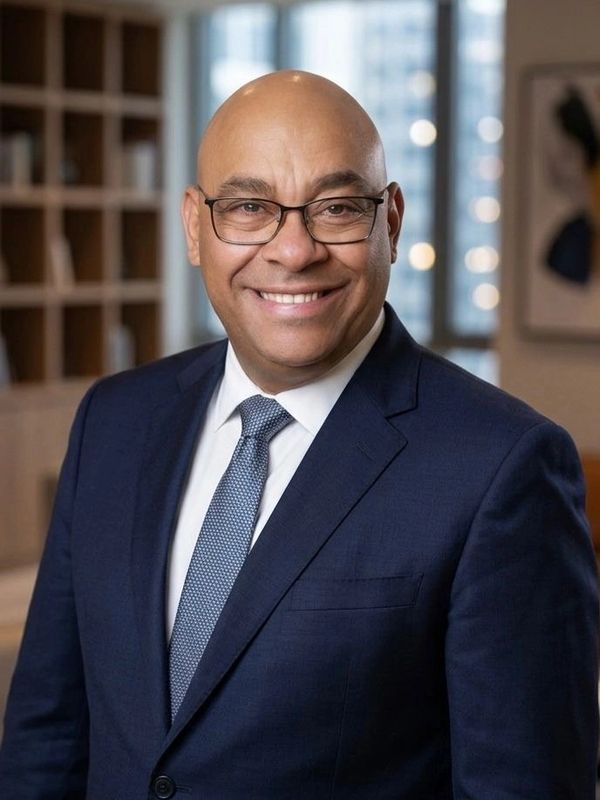 A confident man in glasses and a navy suit smiling indoors.