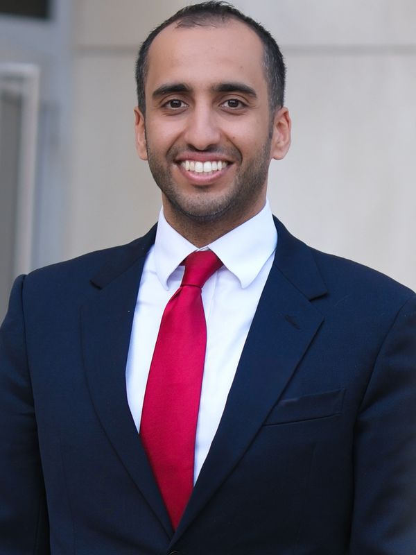 Smiling man in a dark suit with a red tie.
