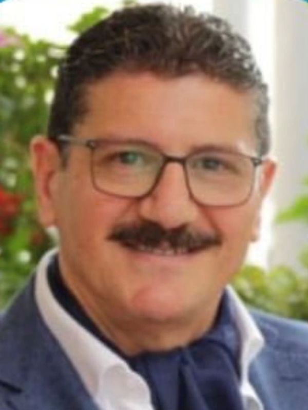 Man with glasses and a mustache smiling outdoors.