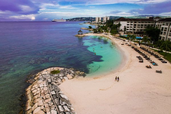 A serene beach with clear waters, lounge chairs, and a cruise ship in the distance.