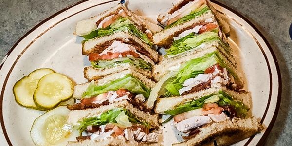 Club sandwiches with lettuce, tomato, and turkey served with pickle slices.