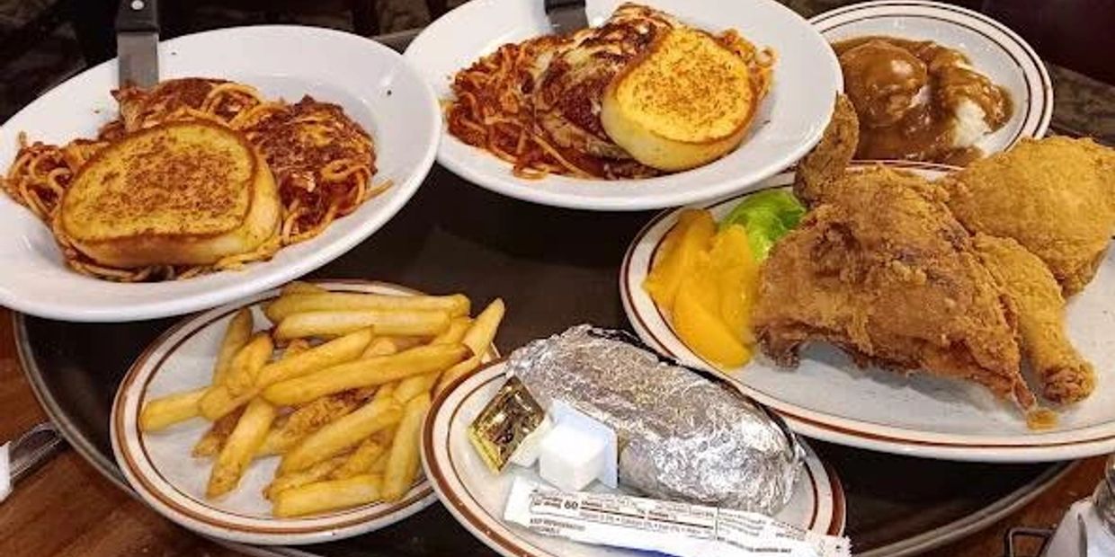 Plates of comfort food with fried chicken, spaghetti, garlic bread, fries, and mashed potatoes with gravy.