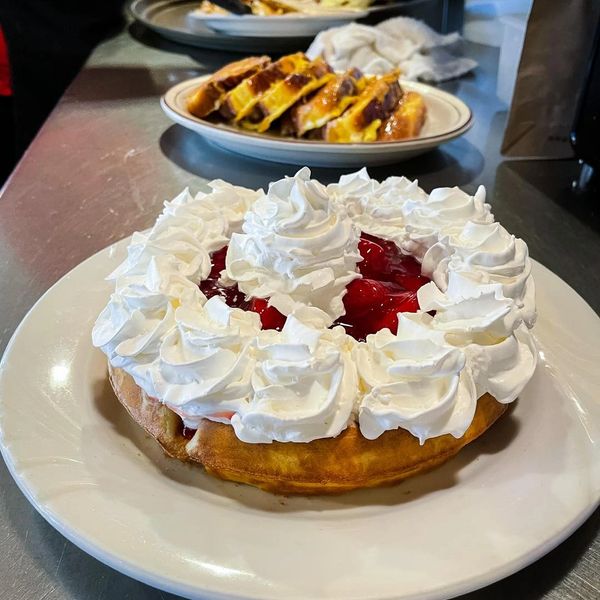Waffle topped with whipped cream and cherry sauce on a white plate.