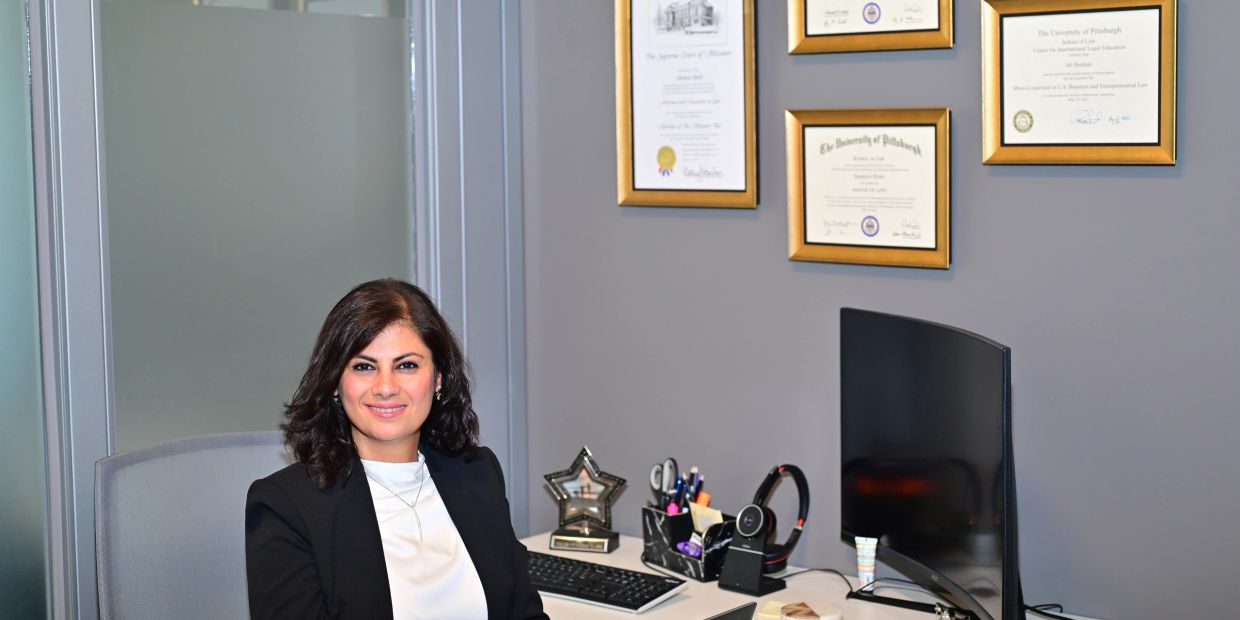 Professional woman sitting at office desk with award and diplomas.