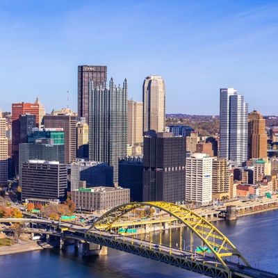 City skyline with a yellow arched bridge over a river on a clear day.