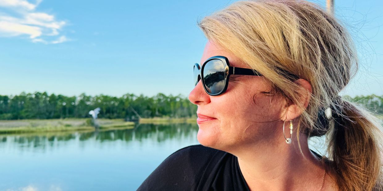 Woman with sunglasses gazing over a serene lake and tree line.