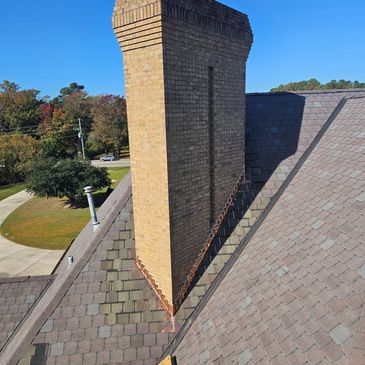 Tall brick chimney on a shingled rooftop under clear blue sky.