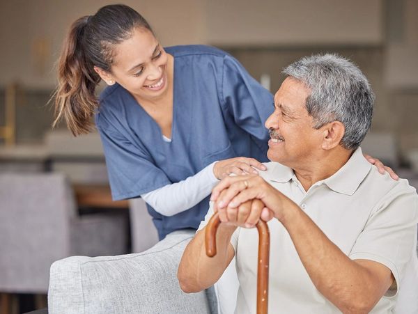A caregiver smiling and comforting an elderly man with a cane.