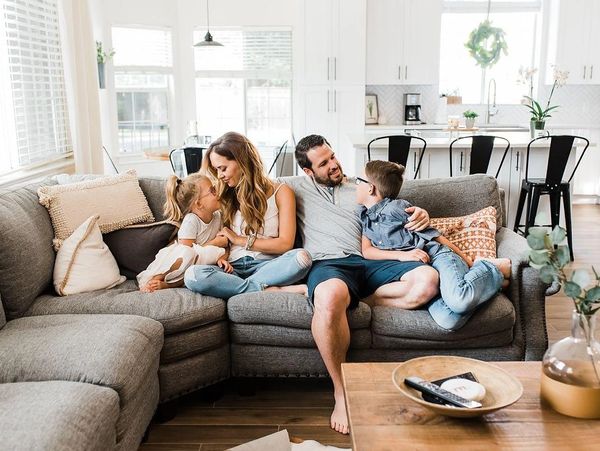 A happy family with two children sitting on a gray couch in a bright living room.