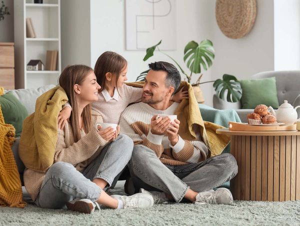 Family enjoying tea together in a cozy living room with muffins on the table.