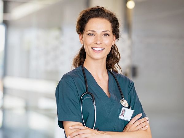 Smiling female nurse in scrubs with stethoscope and ID badge.
