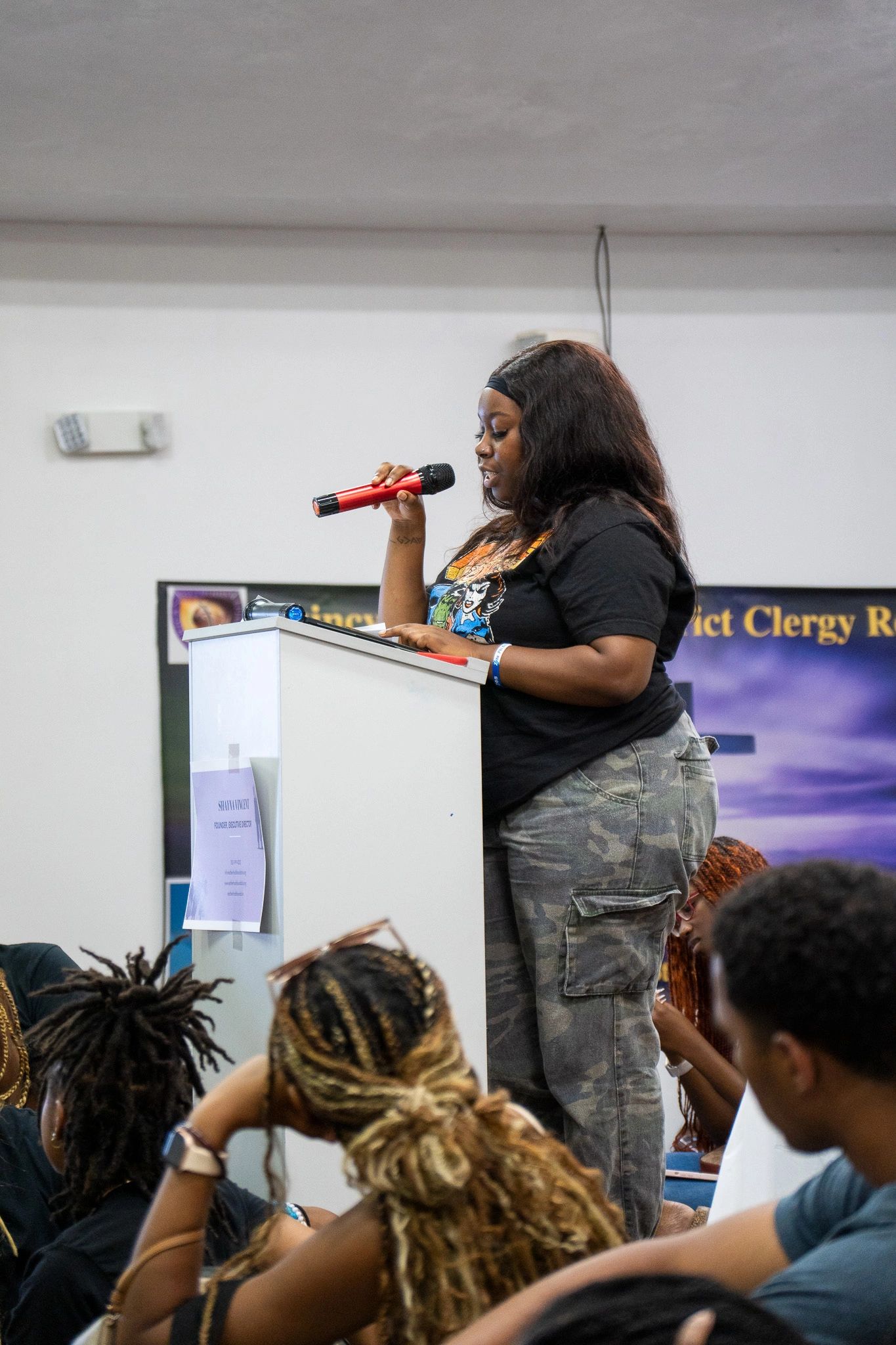 Woman speaking into a red microphone at a podium in front of an audience.