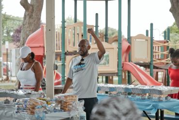 Man speaking at an outdoor event with food tables.