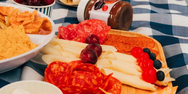 A charcuterie board with salami, cheese, grapes, and berries on a checkered tablecloth.