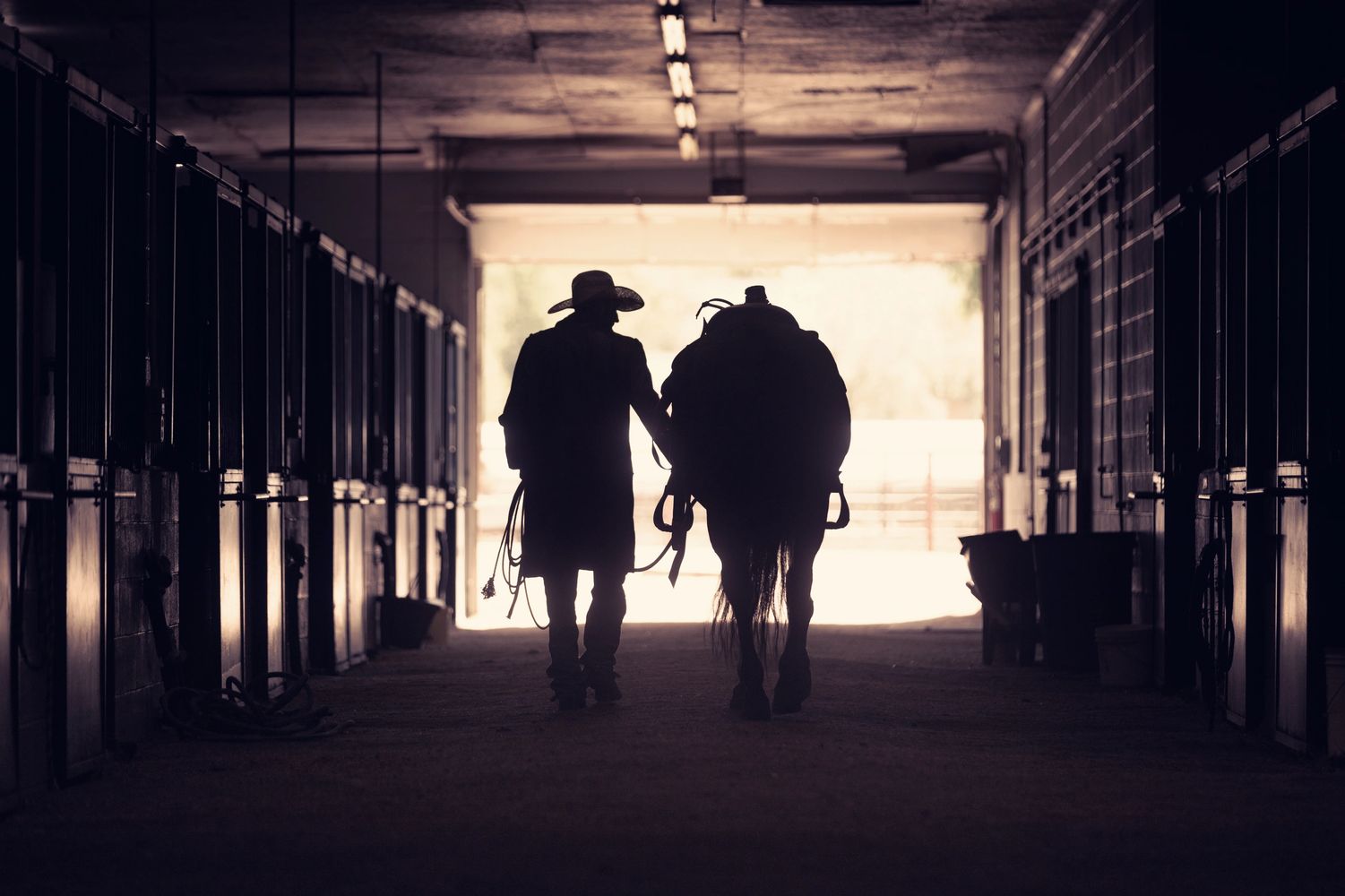 Image of cowboy walking horse out of stables.