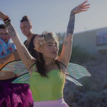 Woman dressed as a fairy with wings and flower headband, dancing outdoors.