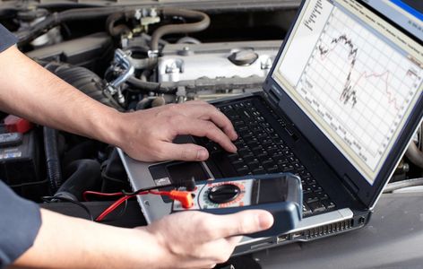 Person using multimeter and laptop for car diagnostics.