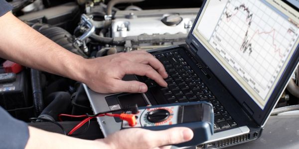 Mechanic using laptop and multimeter to diagnose car.
