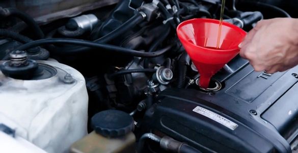 Pouring oil into a car engine using a red funnel.