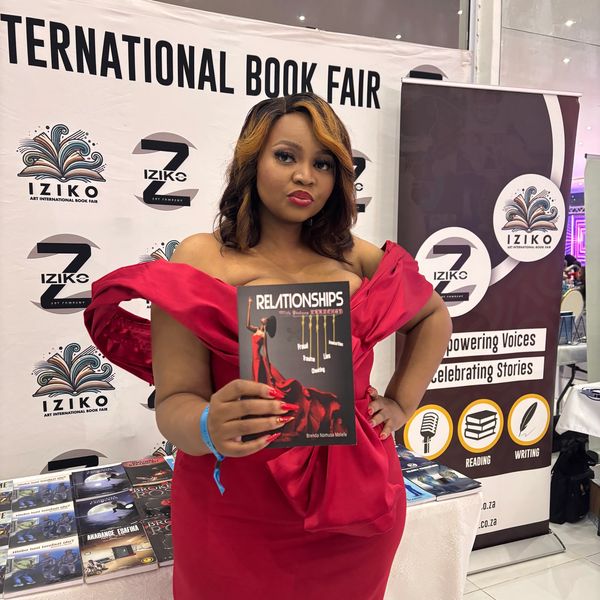 Author in red dress holding her book at the Book Behind awards 2025.