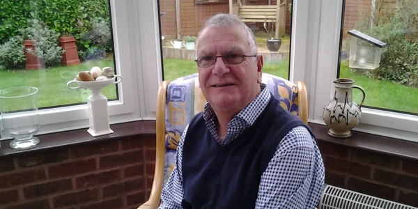 Elderly man sitting in a bright sunroom with a garden view.
