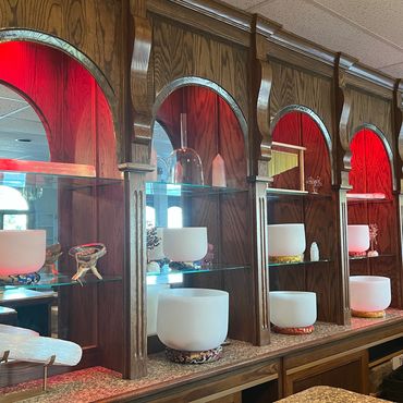 Crystal singing bowls displayed on elegant wooden shelves with red accent lighting.