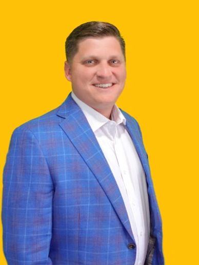 Man in a blue checked blazer and white shirt stands against a yellow background.