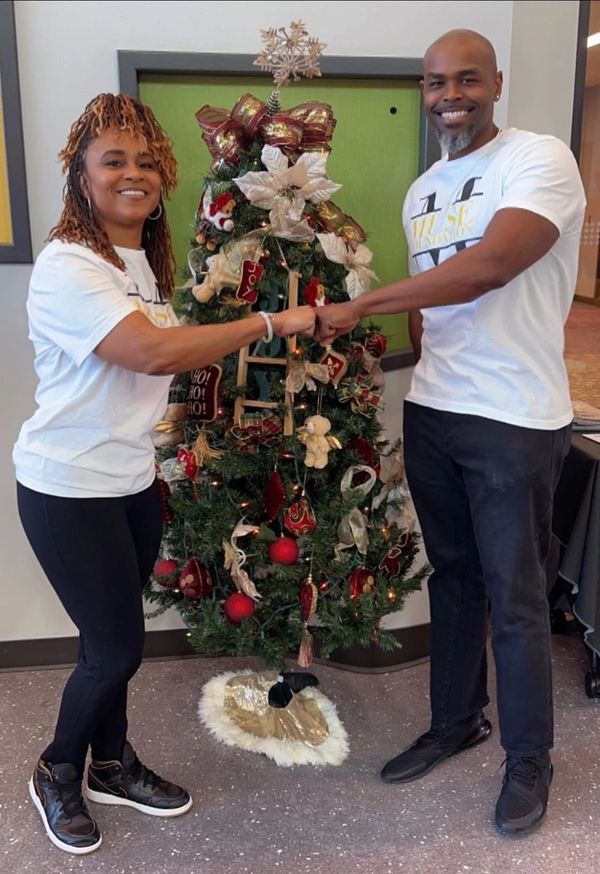 Two people fist bump in front of a decorated Christmas tree indoors.