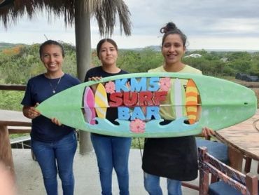 Three women holding a colorful surfboard.