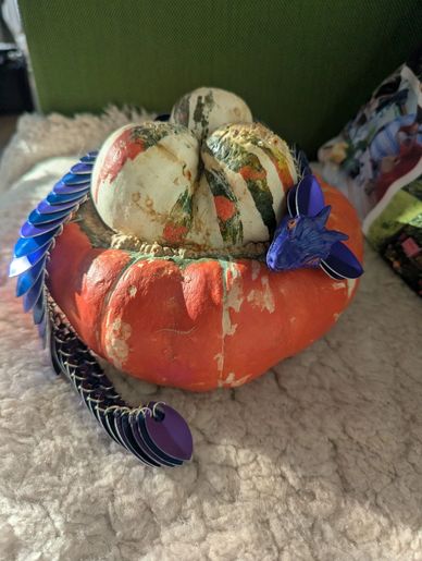 A small, colorful dragon sculpture resting on a two-toned pumpkin.