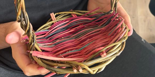Hands holding a woven basket with colored sticks.