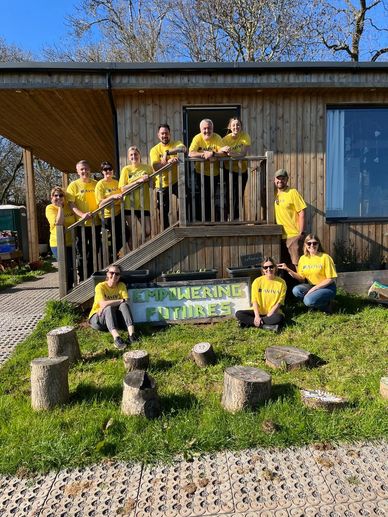 Group of people in yellow shirts posing outside a wooden building with a sign.