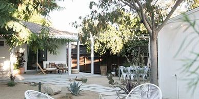 Outdoor seating area with white chairs around a fire pit in a spacious backyard.