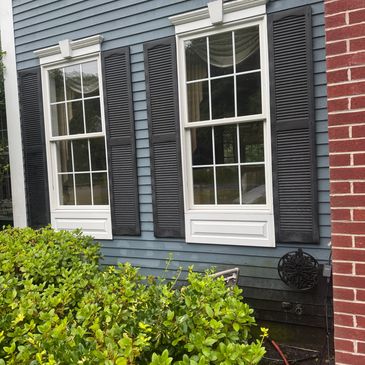 Blue house exterior with two white-framed windows and black shutters.