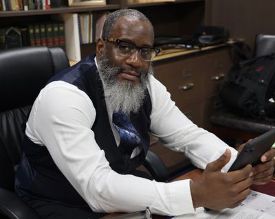 Man with a gray beard in office holding a phone.