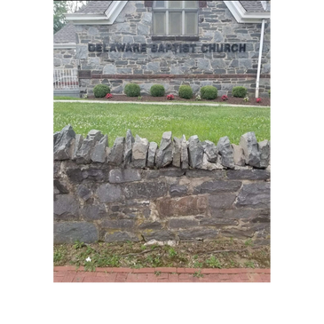 Stone wall and Delaware Baptist Church building with bushes.