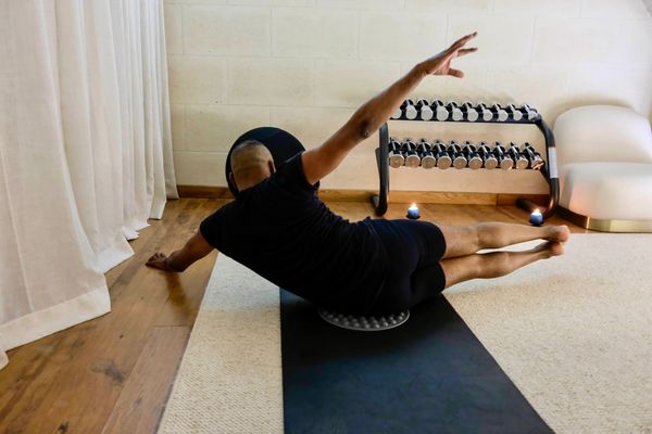 A person performs a workout on a stability roller, extending one arm while balancing on a mat in a w