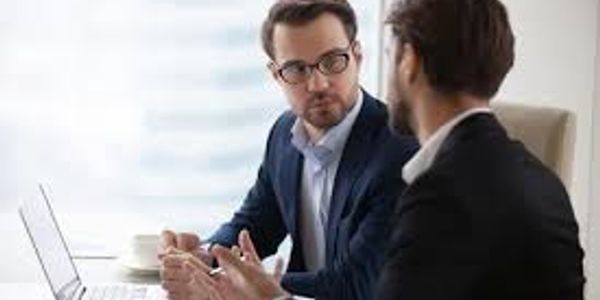 Two businessmen discussing work in an office with a laptop.