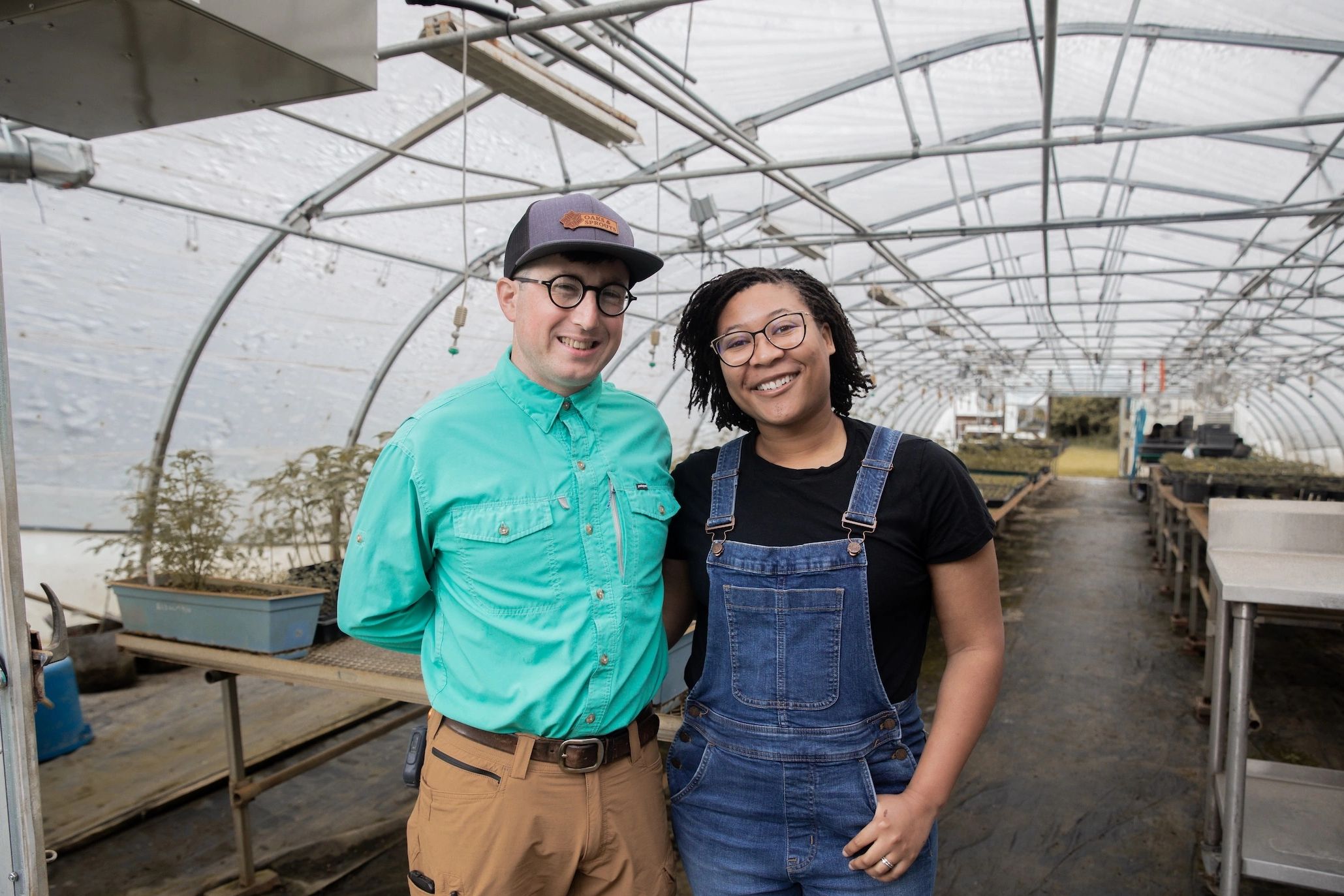 Two gardeners smiling inside a greenhouse.