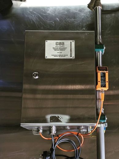 Metal control box mounted on pipes with connected cables.