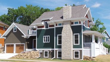 Pop up shed roof dormers and stone chimney chase featuring green siding and cedar shakes