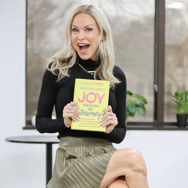 Woman excitedly holds a book titled 'Joy Through the Journey'.