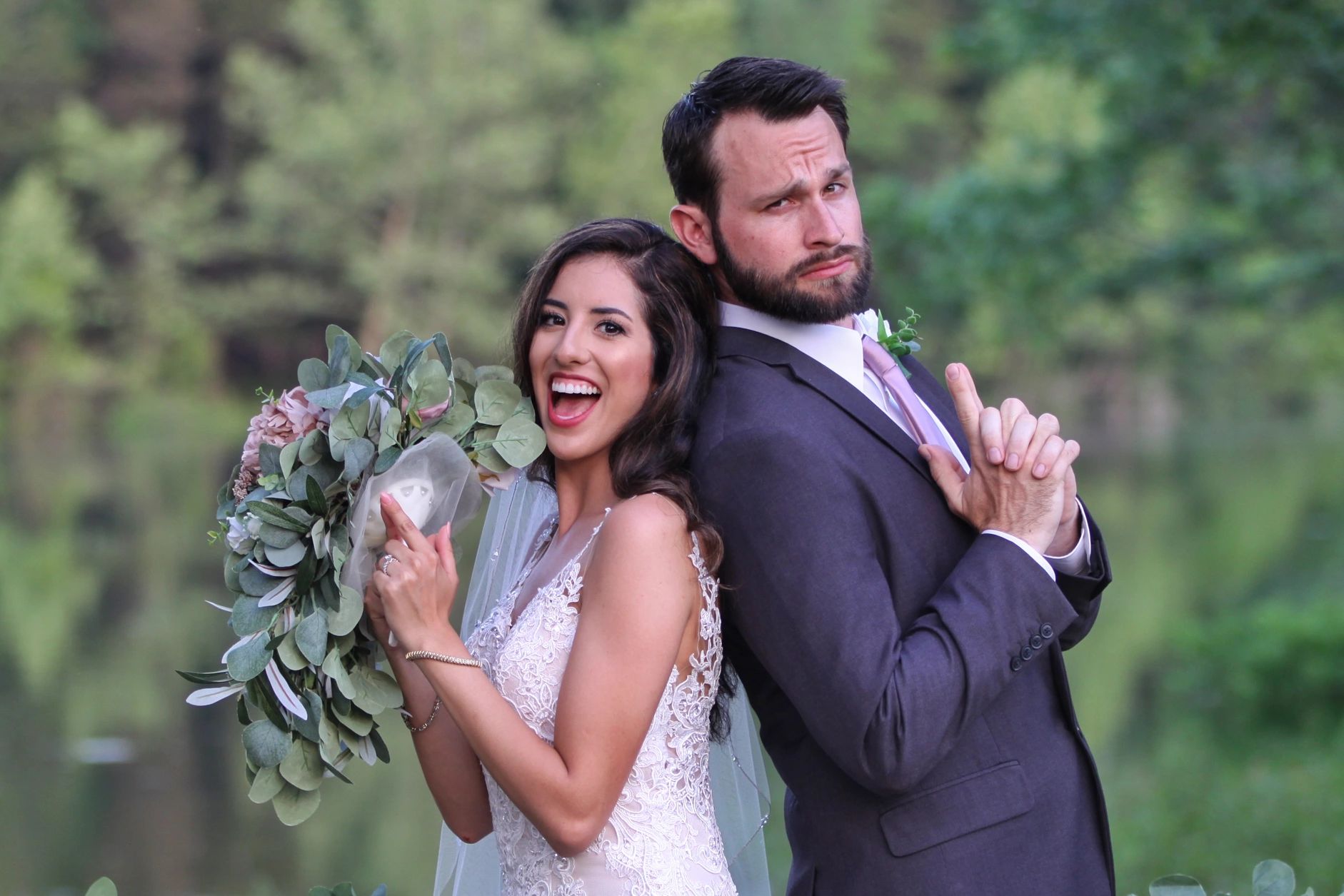 Bride and groom posing playfully back-to-back with finger guns on their wedding day.