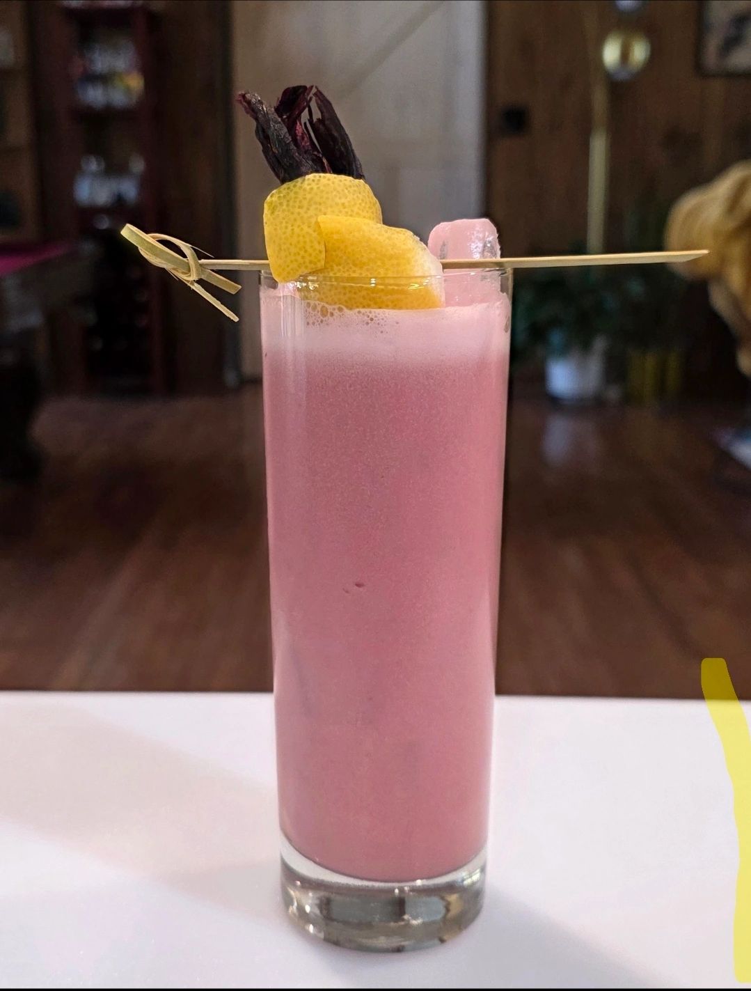 Collins glass filled with the Creamy Hibiscus Lemonade. Its Bright Pink and garnished with a lemon.