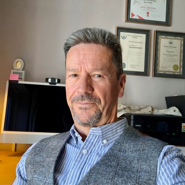 Man in business attire sitting in an office with certificates on the wall.